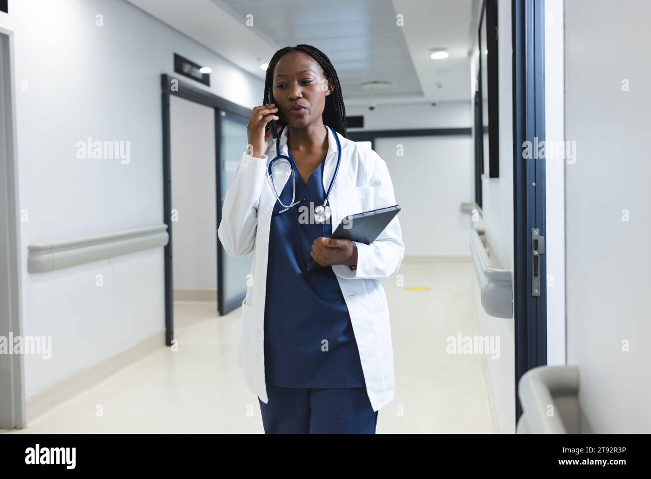 Femme médecin afro-américaine portant une blouse de laboratoire parlant sur smartphone dans le couloir de l'hôpital Banque D'Images