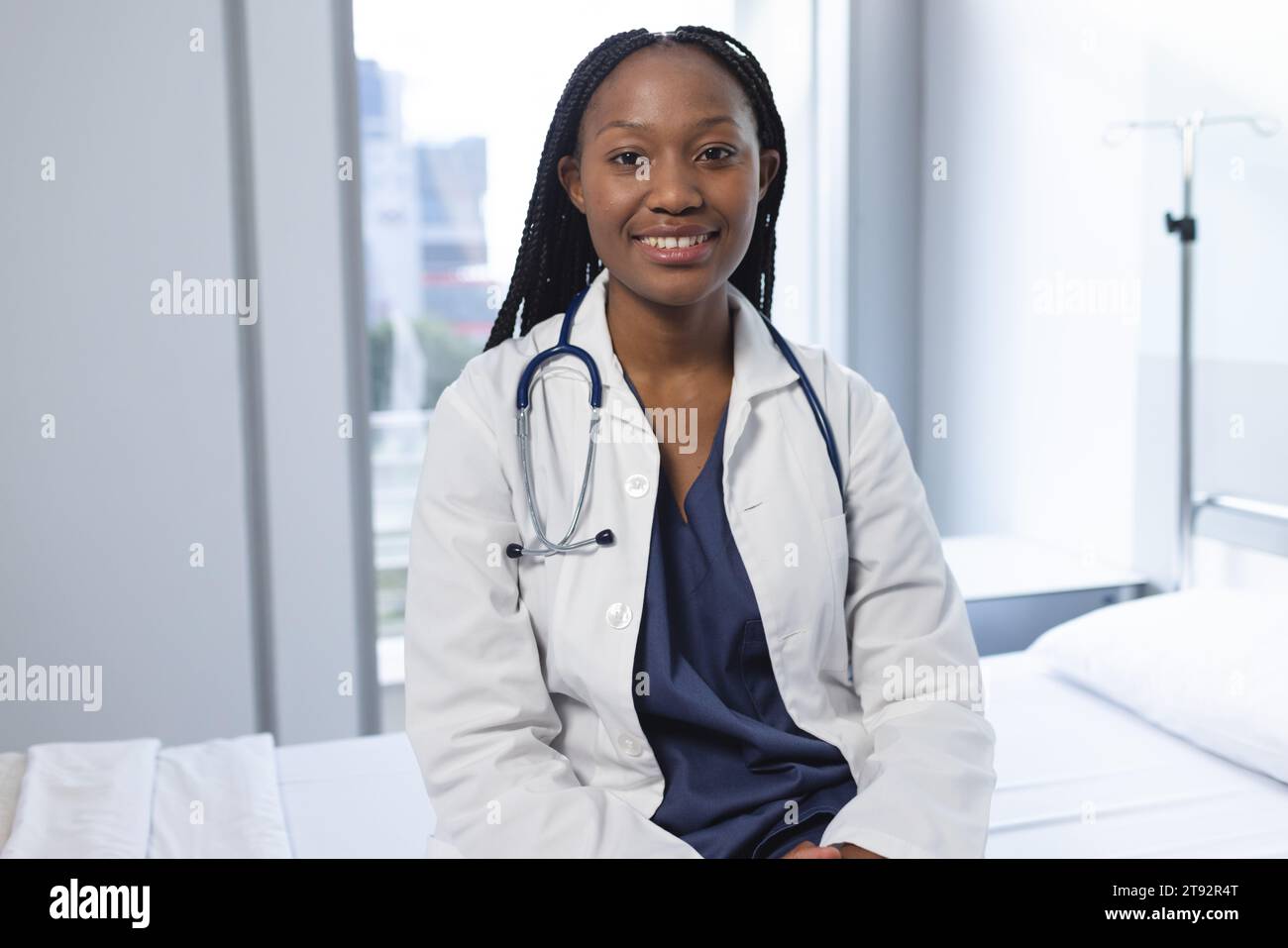 Portrait d'une femme médecin afro-américaine heureuse portant une blouse de laboratoire assise sur le lit dans une chambre d'hôpital Banque D'Images