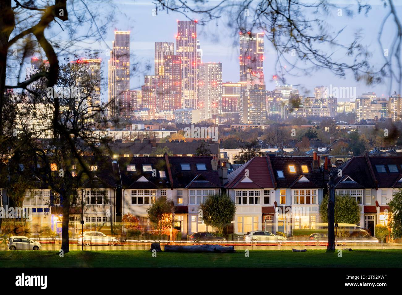 Vu à travers les branches des arbres dans Ruskin Park sont les porches éclairés des maisons d'époque en terrasses et au loin, le développement croissant à Nine Elms à Battersea, le 21 novembre 2023, à Londres, en Angleterre. Banque D'Images