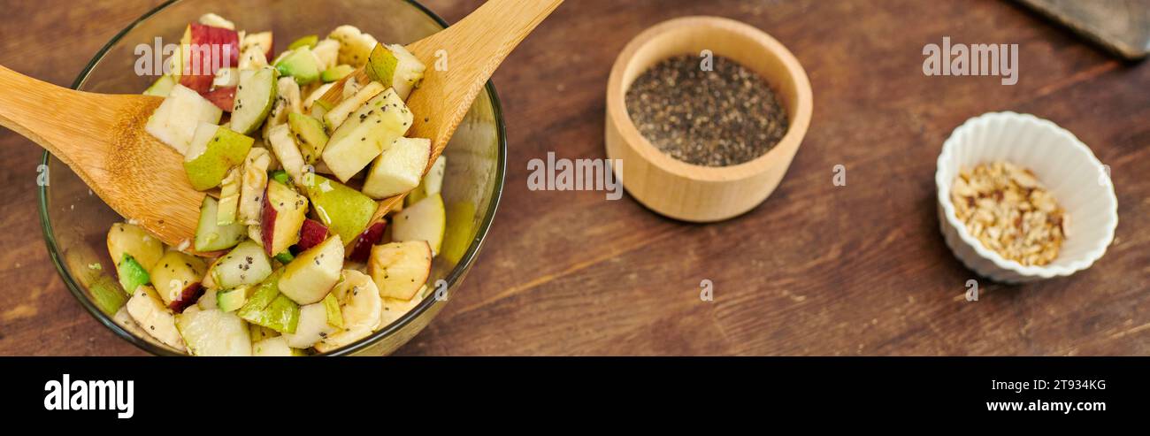 bol en verre avec salade de fruits végétariens et spatules en bois près des graines de sésame et des noix, bannière Banque D'Images