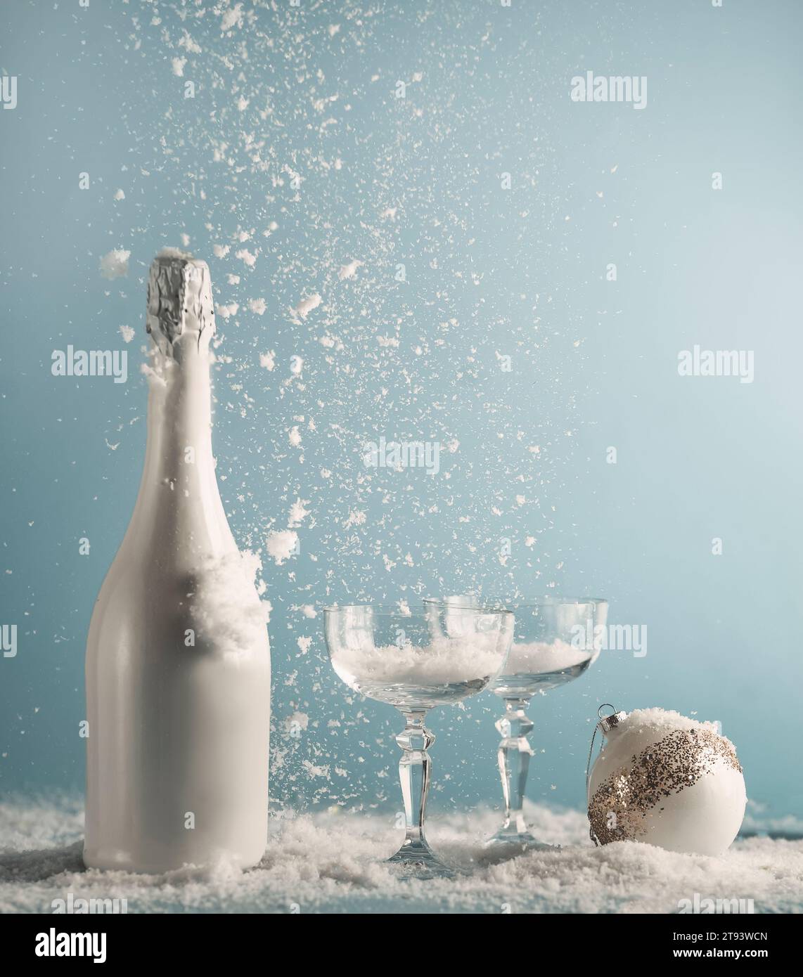 Bouteille de champagne blanche et verres avec boule de Noël sur table avec chute de neige sur fond de mur bleu.Concept du nouvel an avec boisson et chute de neige Banque D'Images