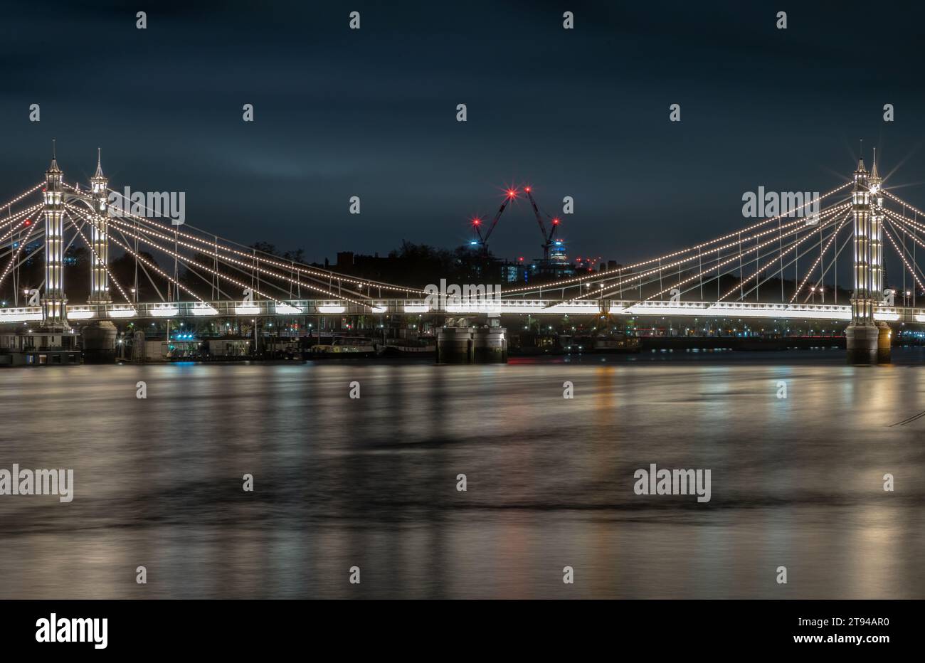 Londres, Royaume-Uni - 20 novembre 2023 - vue nocturne du pont Albert éclairé depuis Chelsea Bridge avec le reflet de la lumière dans une eau très calme. Allumé un Banque D'Images