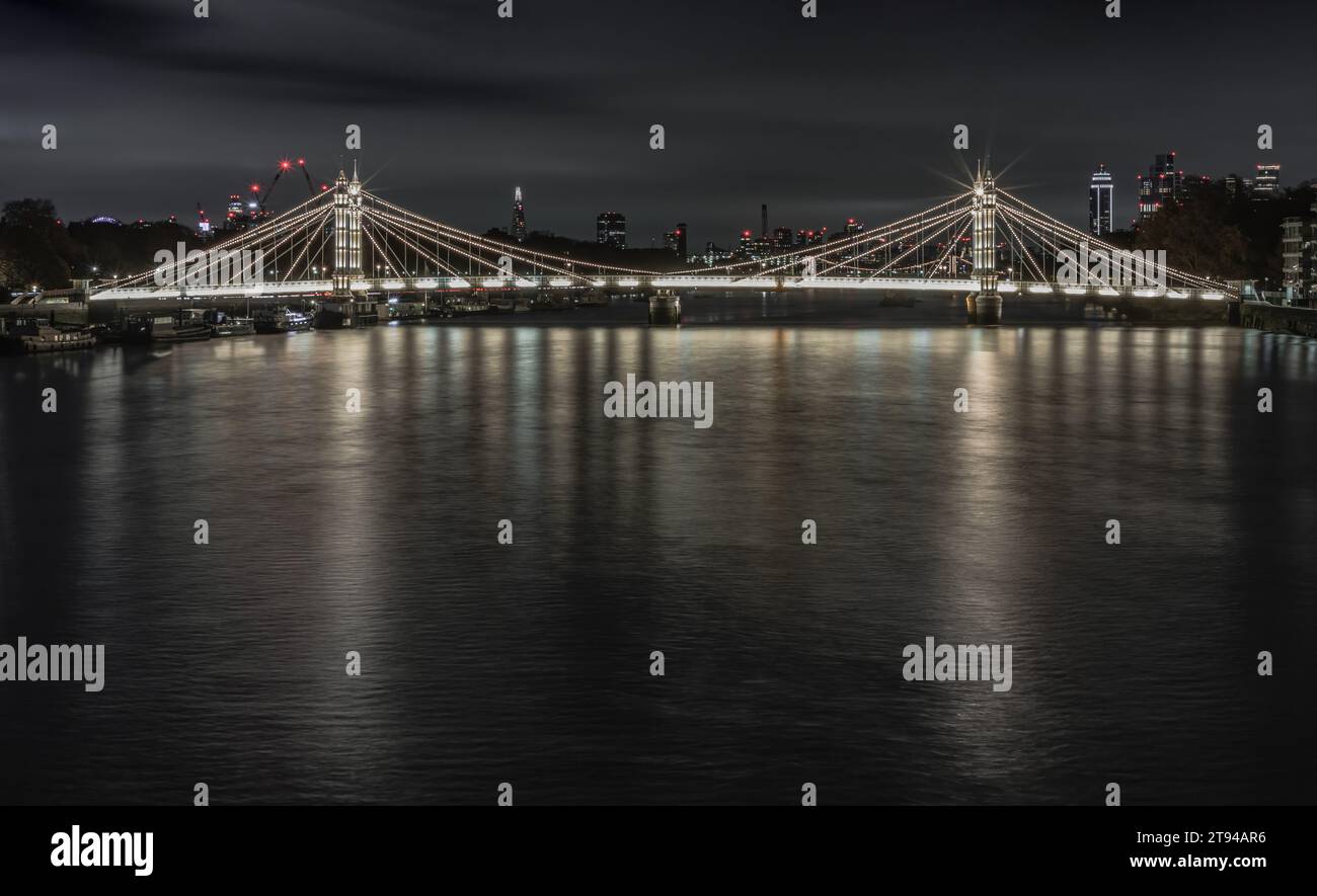 Londres, Royaume-Uni - 20 nov. 2023 - vue nocturne du pont Albert illuminé depuis Chelsea Bridge avec le reflet de la lumière dans l'eau très calme de la rivière Banque D'Images