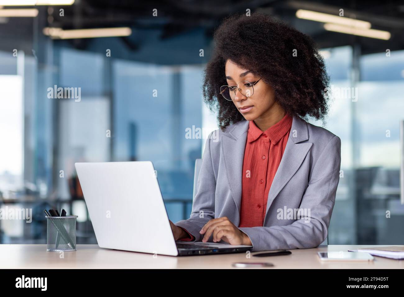 Une jeune femme d'affaires afro-américaine est assise à un bureau dans le bureau et se concentre sur le travail sur un ordinateur portable. Banque D'Images