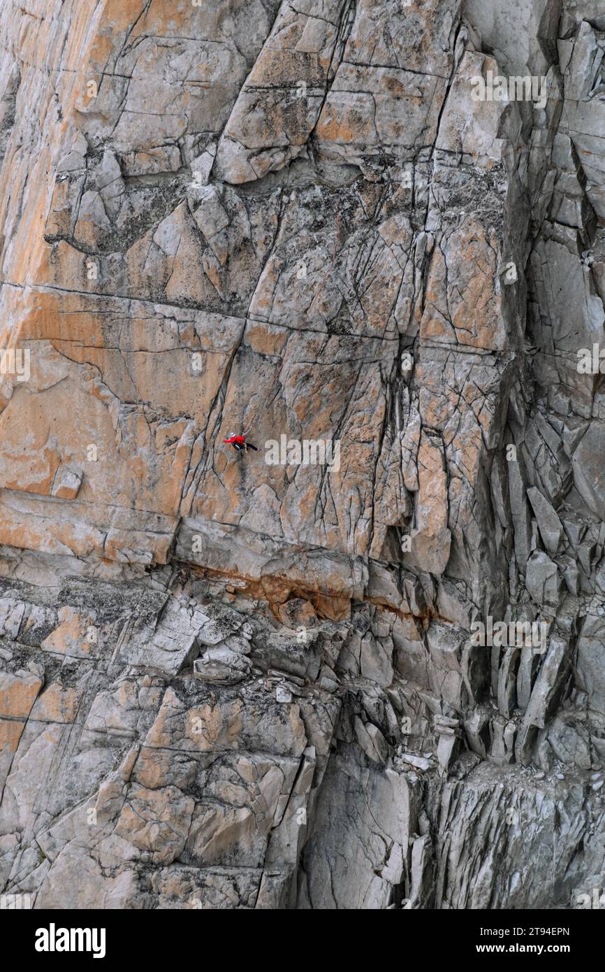 Chamonix, France - 25 août 2023 : un seul grimpeur de roche sécurisé avec une corde supérieure atteignant pour l'adhérence sur la grande paroi rocheuse verticale de montagne dans les Alpes Banque D'Images