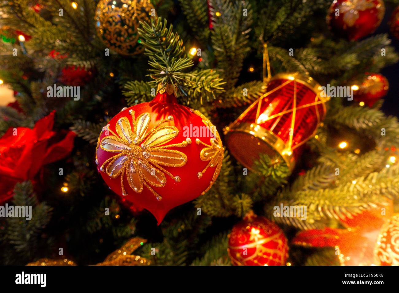 Boule de Noël rouge et or ornée de détails scintillants sur fond vert chaud d'arbre de Noël flou Banque D'Images