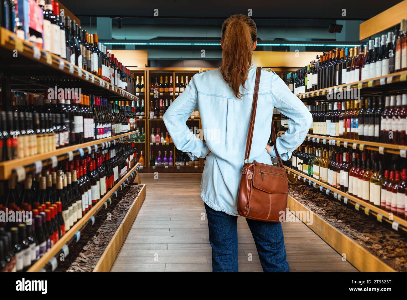 Vue arrière de la femme consommateur debout dans le magasin d'alcool et choisit le vin. Banque D'Images