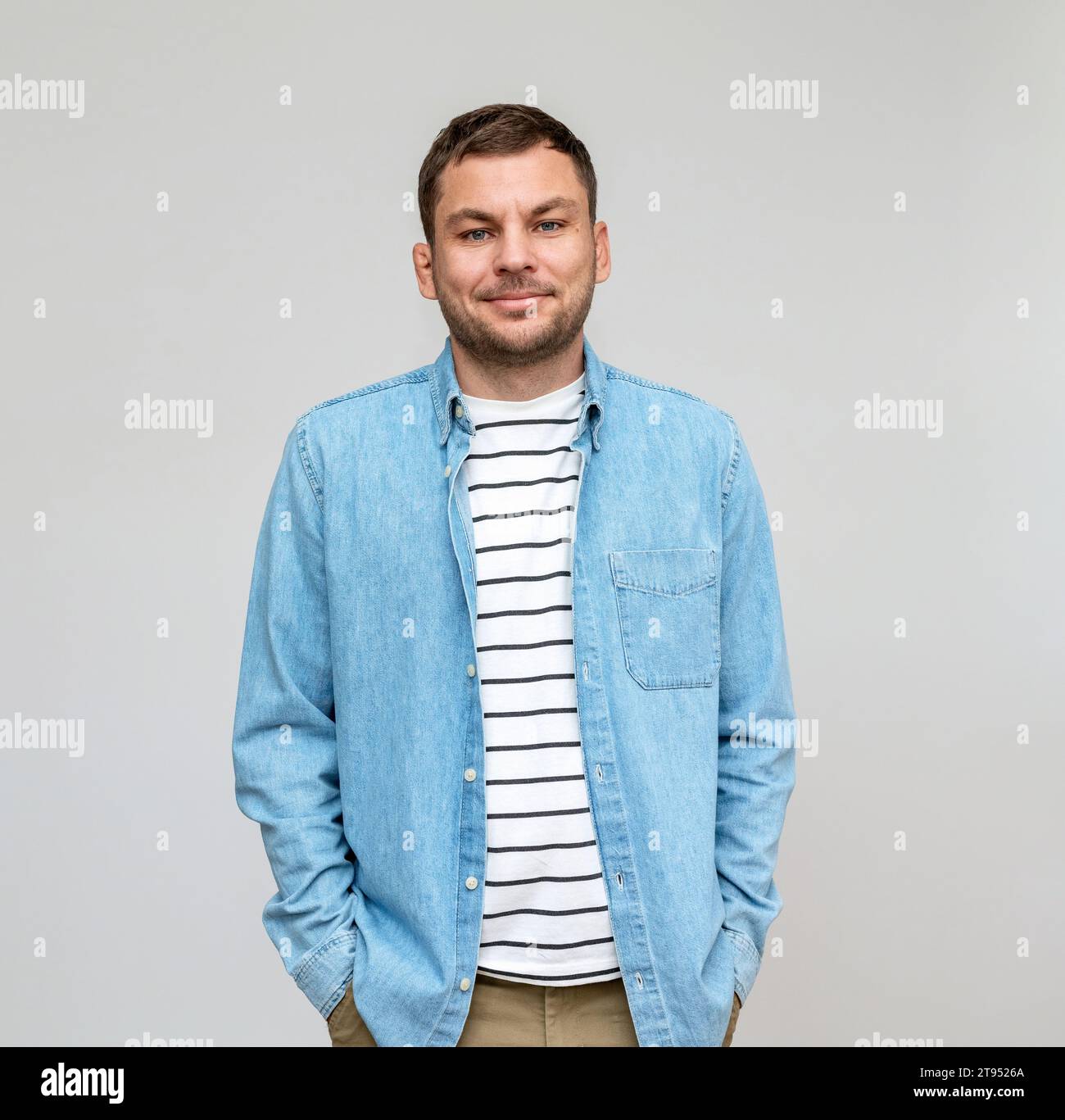 Portrait d'homme décontracté portant en jeans chemise et t-shirt rayé sourit devant le fond Uni en studio. Banque D'Images