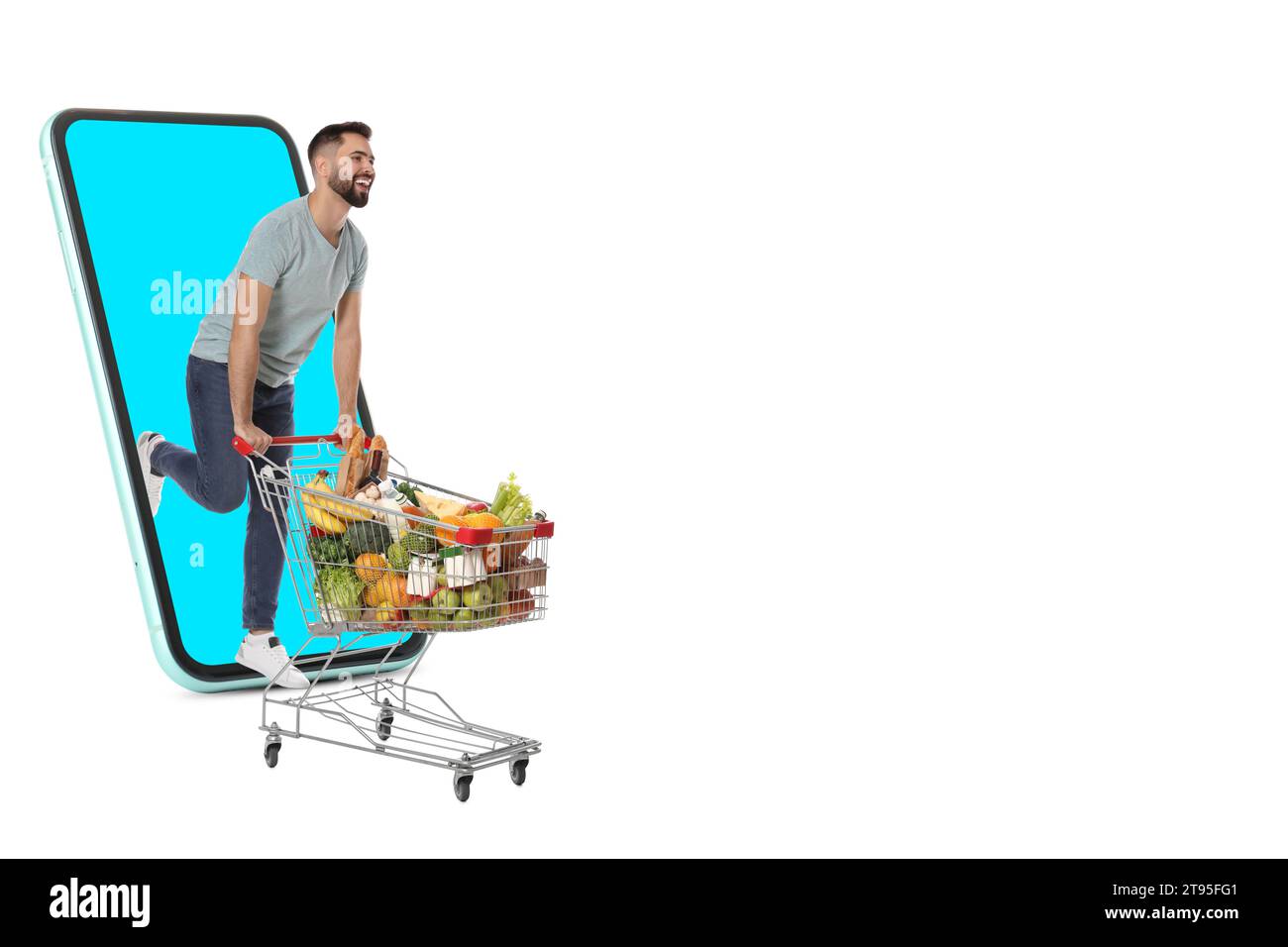 Épicerie via Internet. Homme heureux avec panier plein de produits à court d'énorme smartphone sur fond blanc Banque D'Images