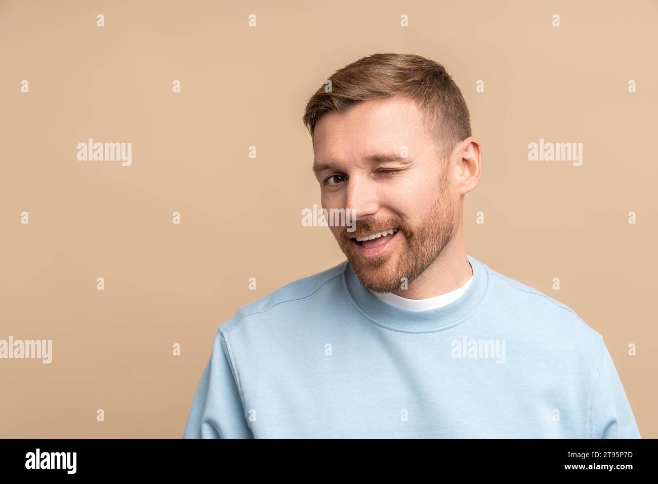 Flirter homme clin d'œil, regarder la caméra, portrait de studio isolé sur beige. Ludique et impitoyable, insinuant. Banque D'Images