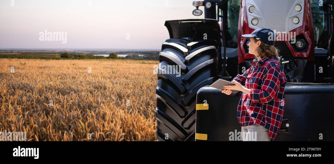 Agricultrice avec une tablette numérique à côté du tracteur agricole. Banque D'Images