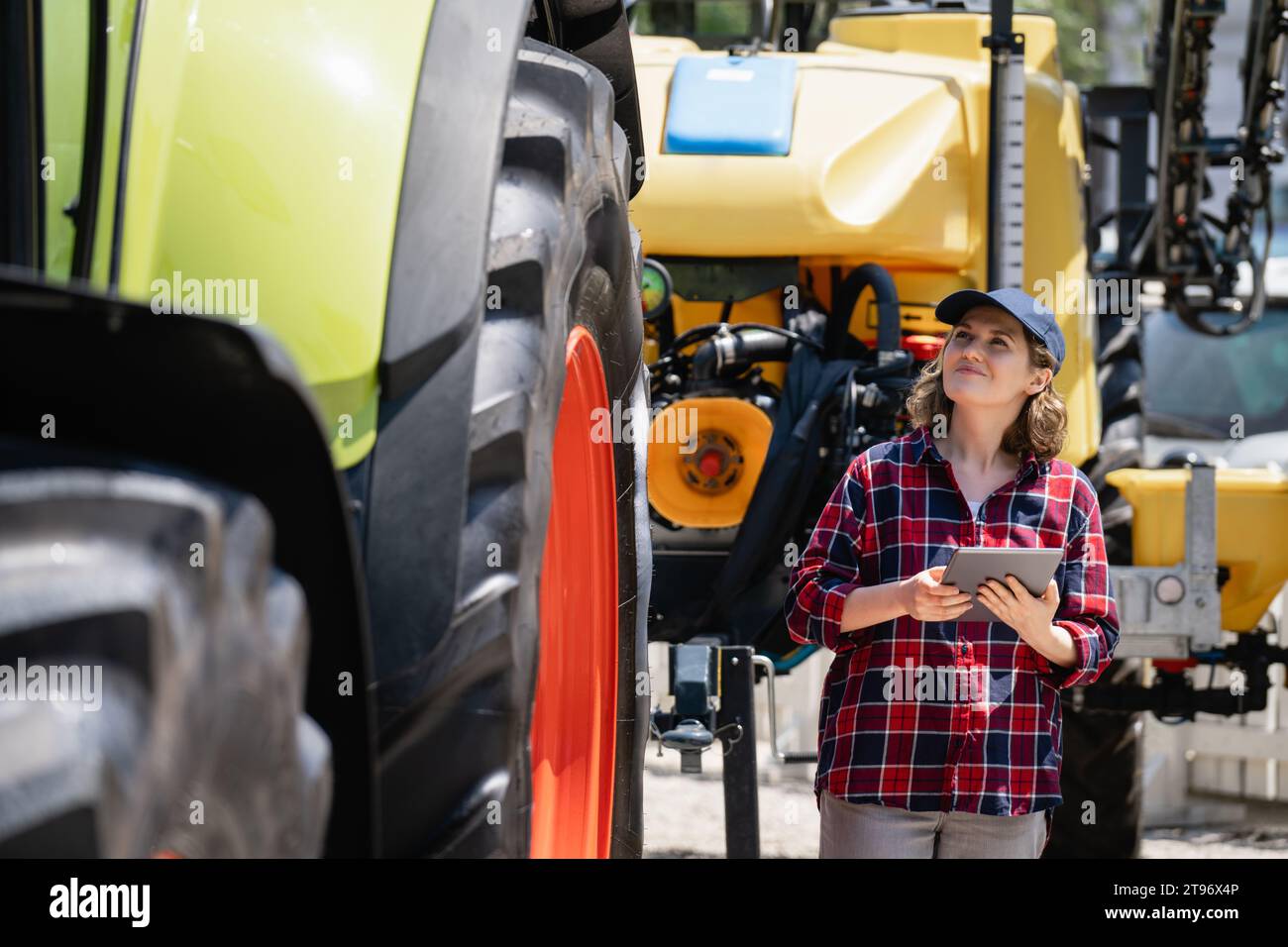 Agricultrice avec une tablette numérique à côté du tracteur agricole. Banque D'Images