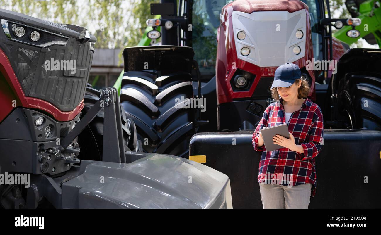 Agricultrice avec une tablette numérique à côté du tracteur agricole. Banque D'Images