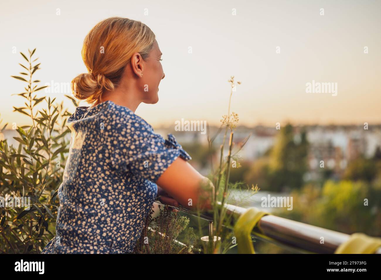 Belle femme aime se tenir debout sur son balcon au coucher du soleil. Banque D'Images