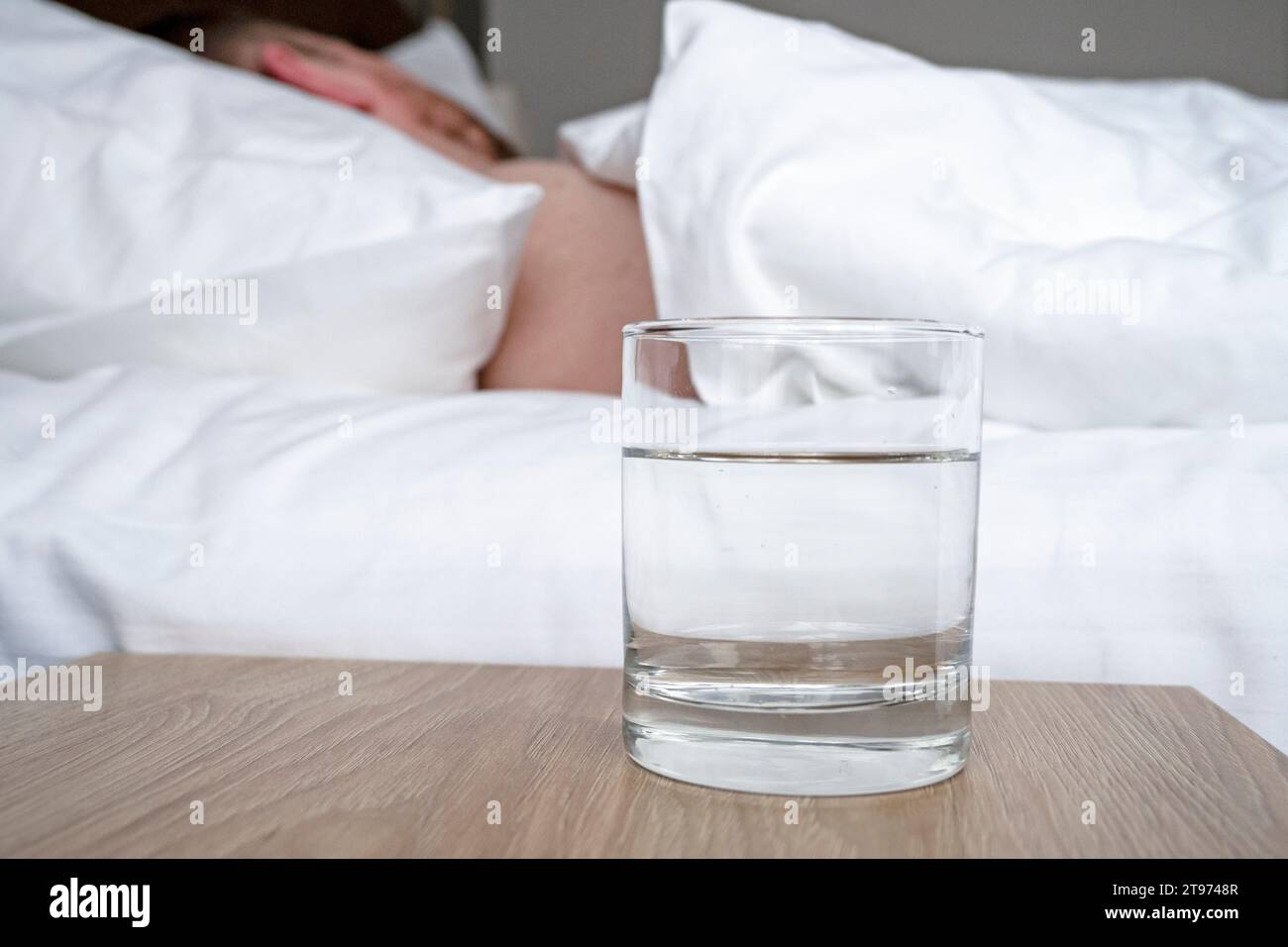 Verre avec de l'eau sur une table en bois et personne à coucher dans une chambre Banque D'Images