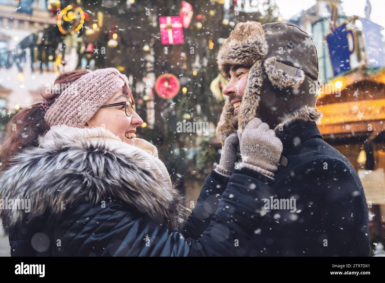 Couple en tenue d'hiver souriant l'un à l'autre, lors d'une journée d'hiver enneigée à un marché de noël Banque D'Images