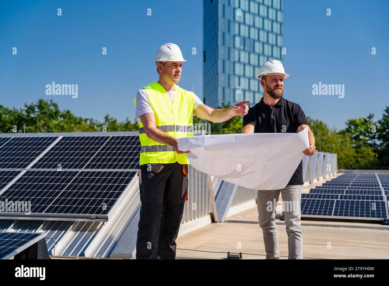 Deux techniciens élaborent des stratégies sur le toit d’un immeuble corporatif orné de panneaux solaires Banque D'Images