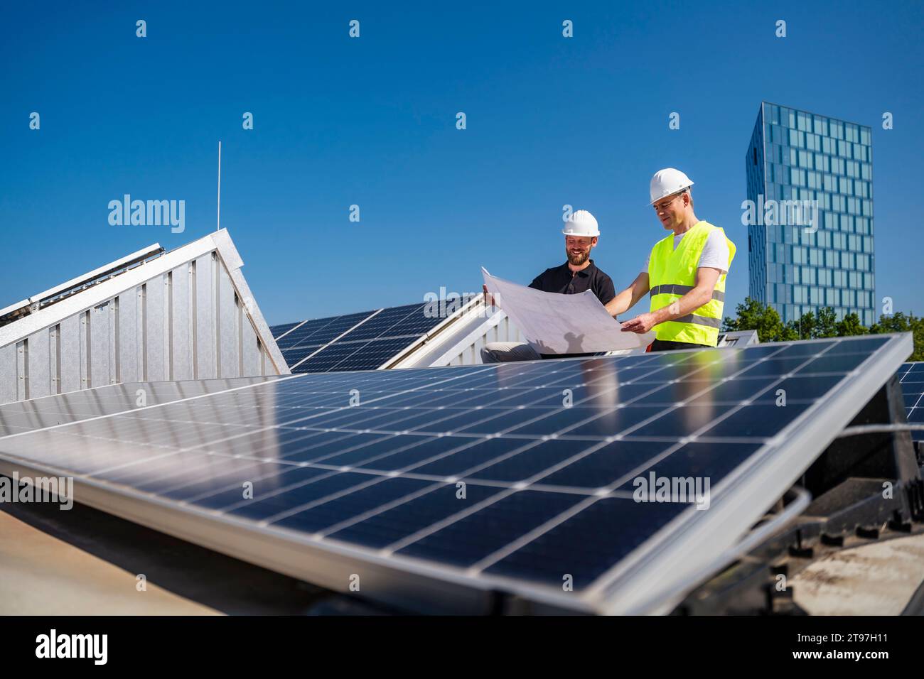 Deux techniciens élaborent des stratégies sur le toit d'un bâtiment d'entreprise alimenté à l'énergie solaire Banque D'Images
