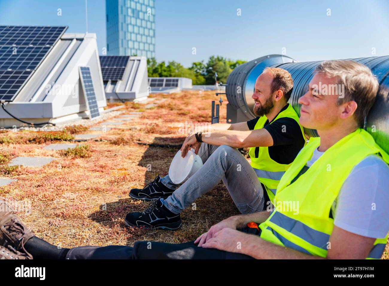 Deux techniciens profitant d’une pause sur le toit d’un bâtiment de l’entreprise, entourés de panneaux solaires Banque D'Images