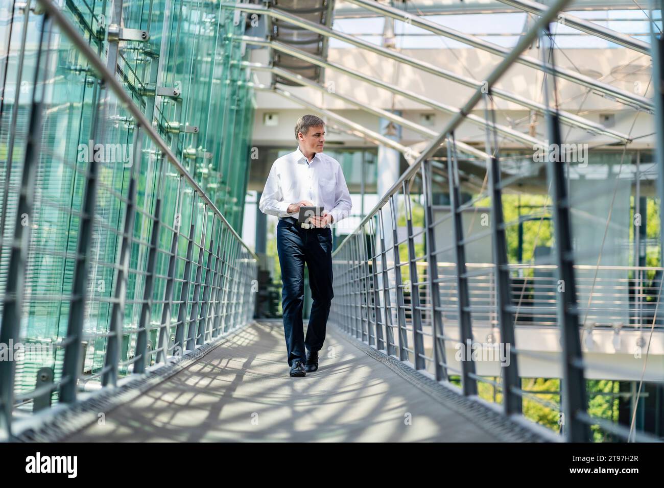 Homme d'affaires marchant dans le couloir de l'immeuble de bureaux moderne en utilisant la tablette numérique Banque D'Images