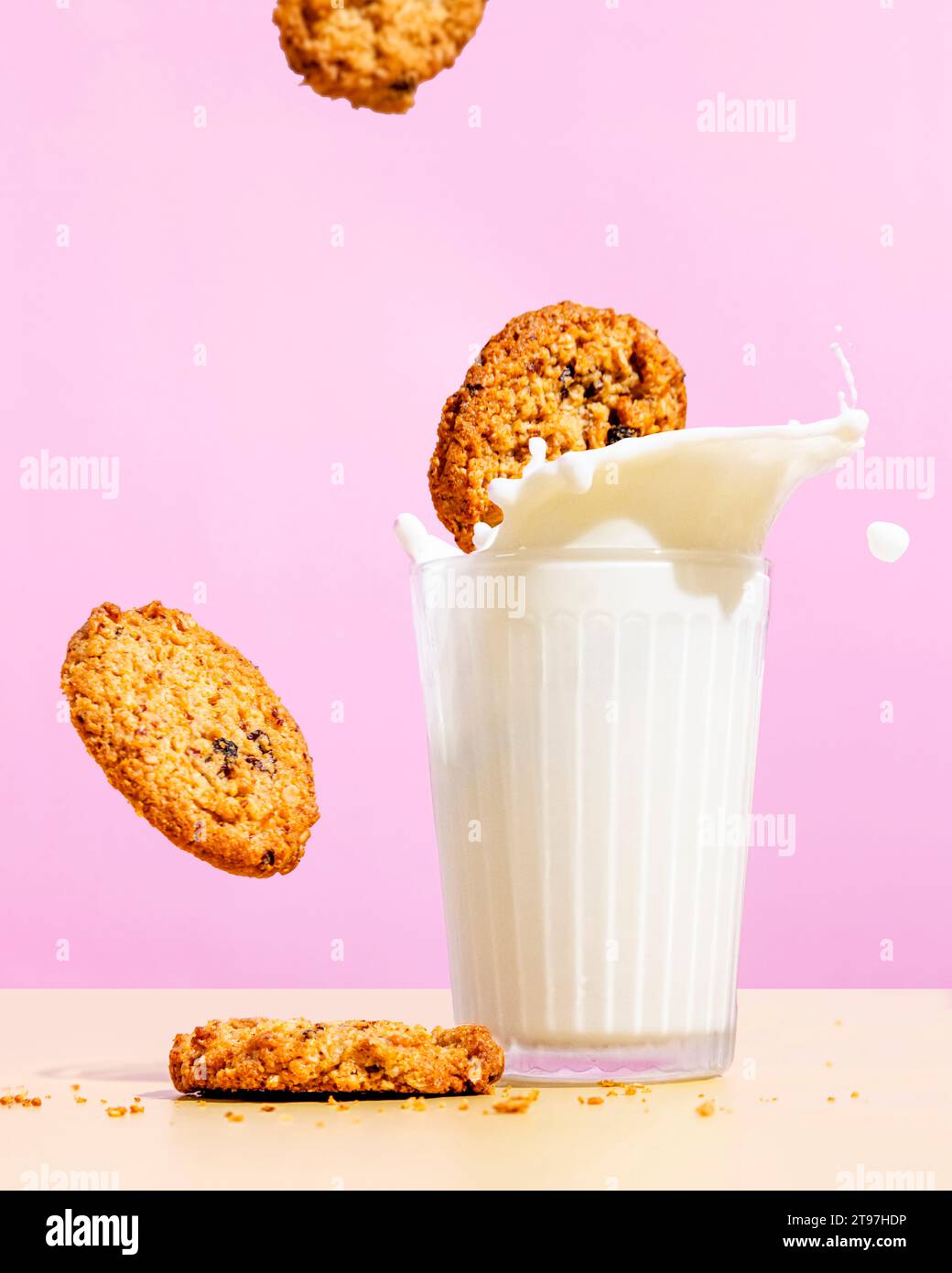 Cookies volants à la farine d'avoine près du lait éclaboussant dans le verre sur fond de couleur rose Banque D'Images