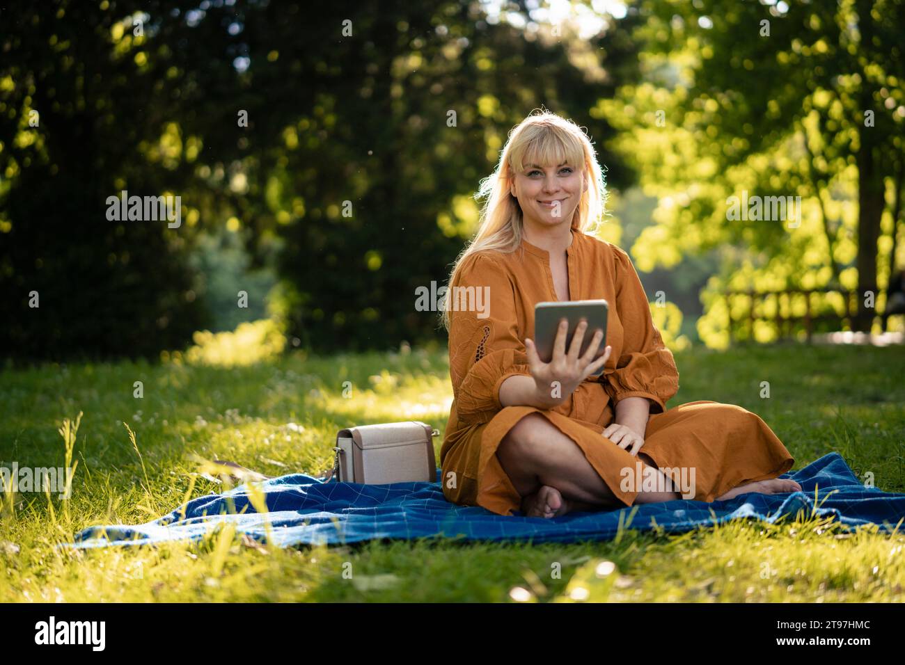 Femme souriante assise sur une couverture avec tablette PC dans le parc Banque D'Images