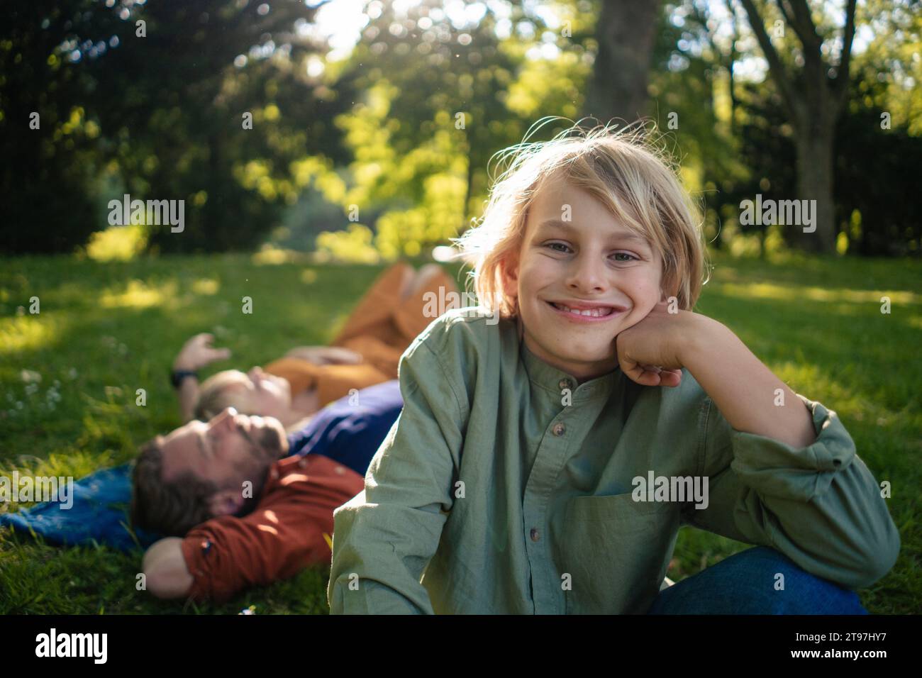 Garçon souriant avec des parents en arrière-plan se relaxant dans le parc Banque D'Images