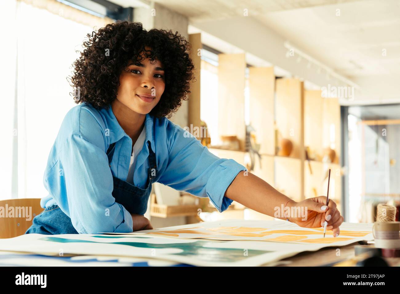 Artiste avec la peinture de cheveux bouclés avec la brosse au bureau dans le studio Banque D'Images