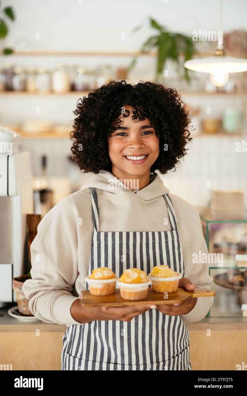 Joyeux barista tenant des cupcakes sur une planche à découper dans un café Banque D'Images