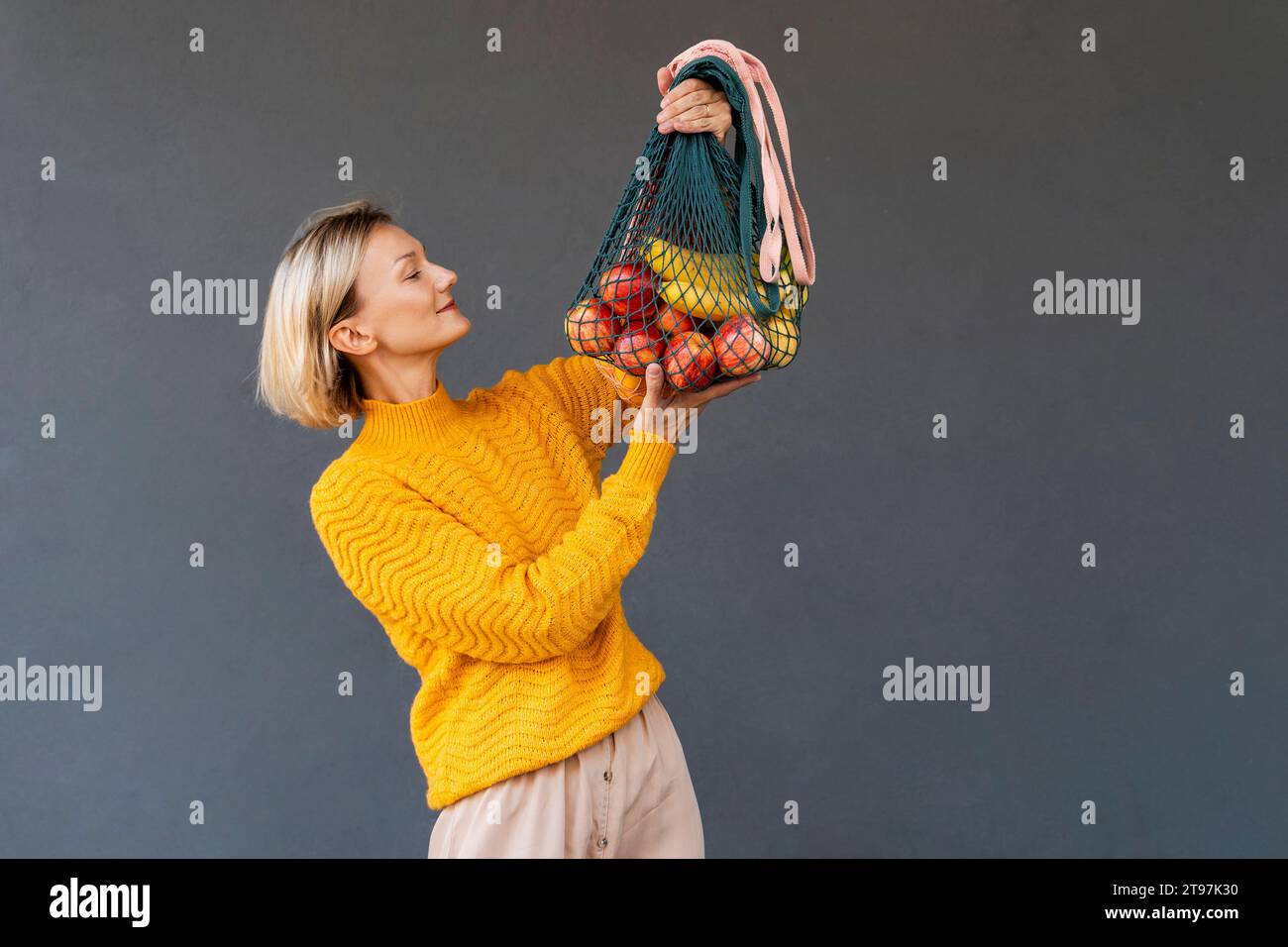 Femme souriante regardant des sacs en maille avec des fruits sur fond noir Banque D'Images