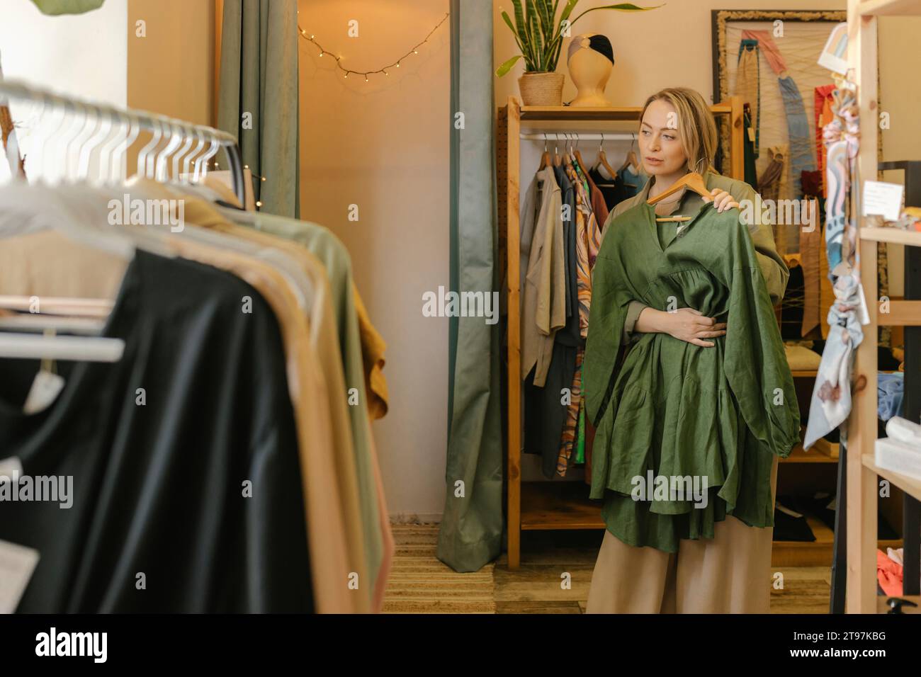 Femme blonde tenant la robe et debout près du porte-vêtements au magasin Banque D'Images