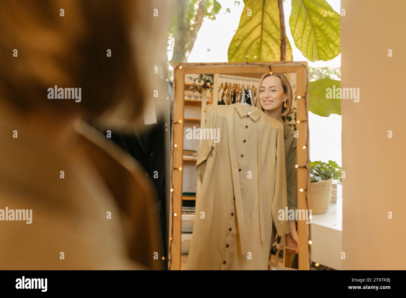 Femme souriante essayant sur la robe et regardant le miroir dans le magasin Banque D'Images