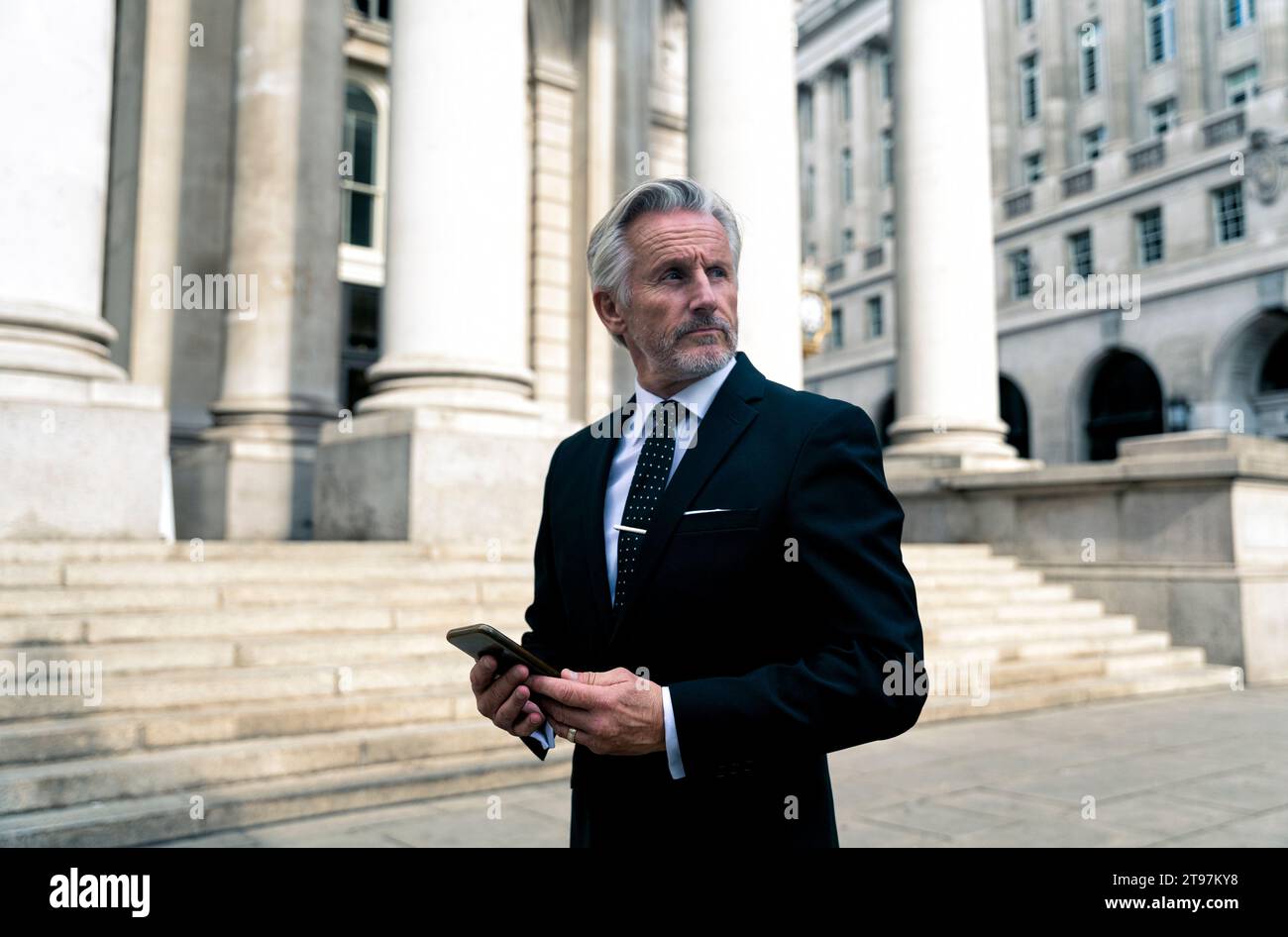 Homme d'affaires senior debout avec téléphone intelligent près du bâtiment Banque D'Images