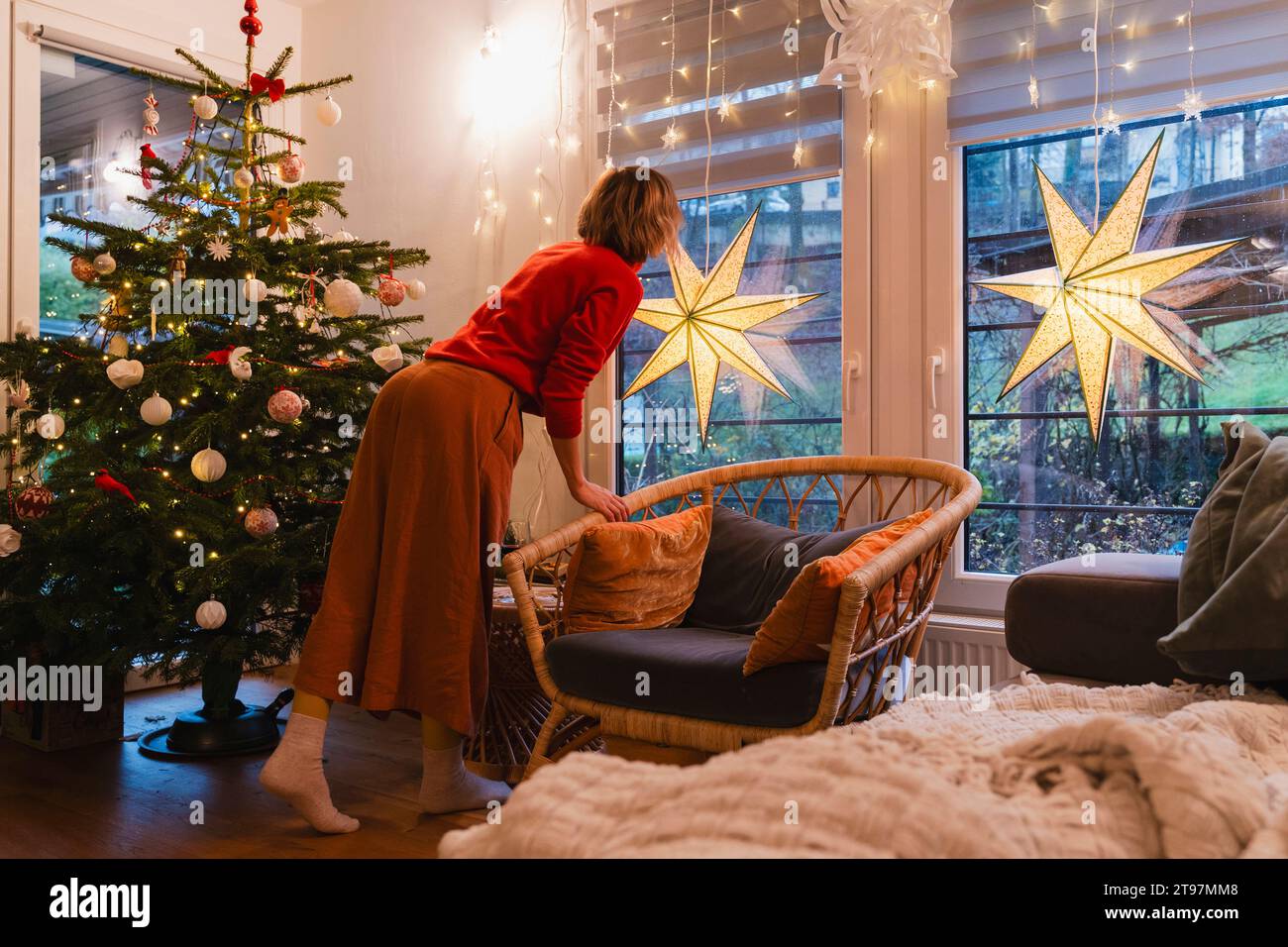 Femme debout près de l'arbre de Noël et regardant par la fenêtre à la maison Banque D'Images