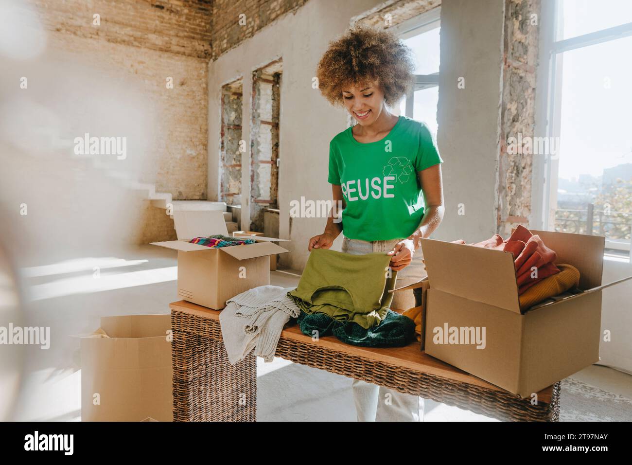 Sourire activiste pliant des vêtements près de la boîte de don dans l'appartement Banque D'Images