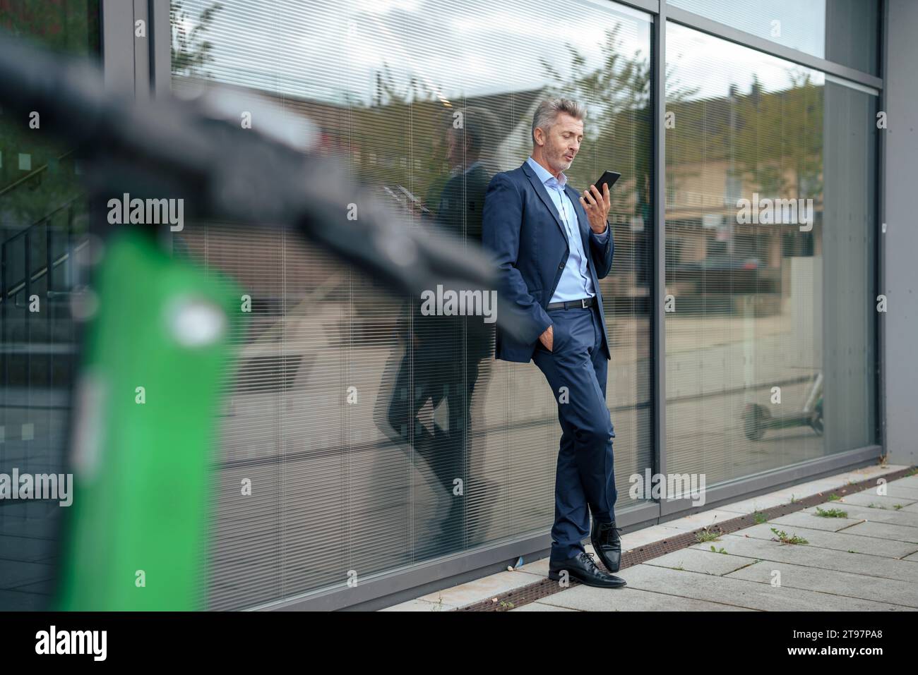 Homme d'affaires mature utilisant un téléphone intelligent et se penchant sur le verre au sentier Banque D'Images