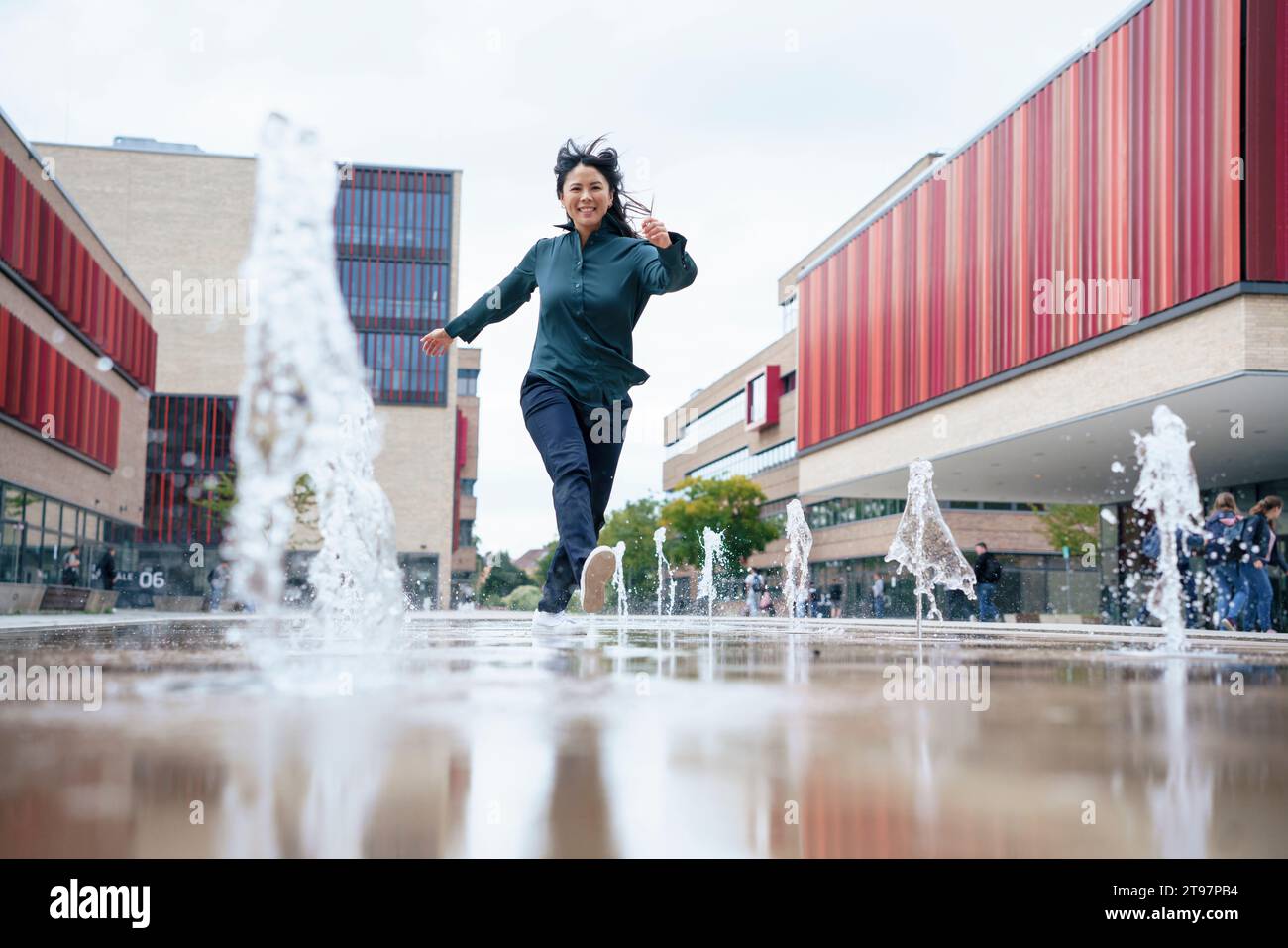 Joyeuse femme d'affaires courant près des fontaines d'eau dans le parc de bureaux Banque D'Images