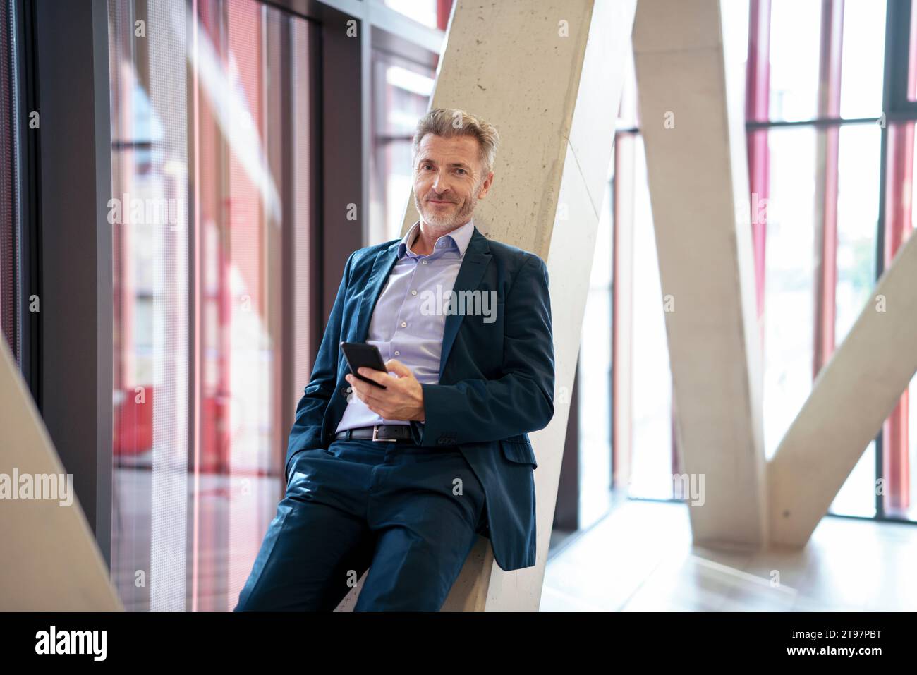 Homme d'affaires mûr souriant avec téléphone intelligent appuyé sur la colonne Banque D'Images