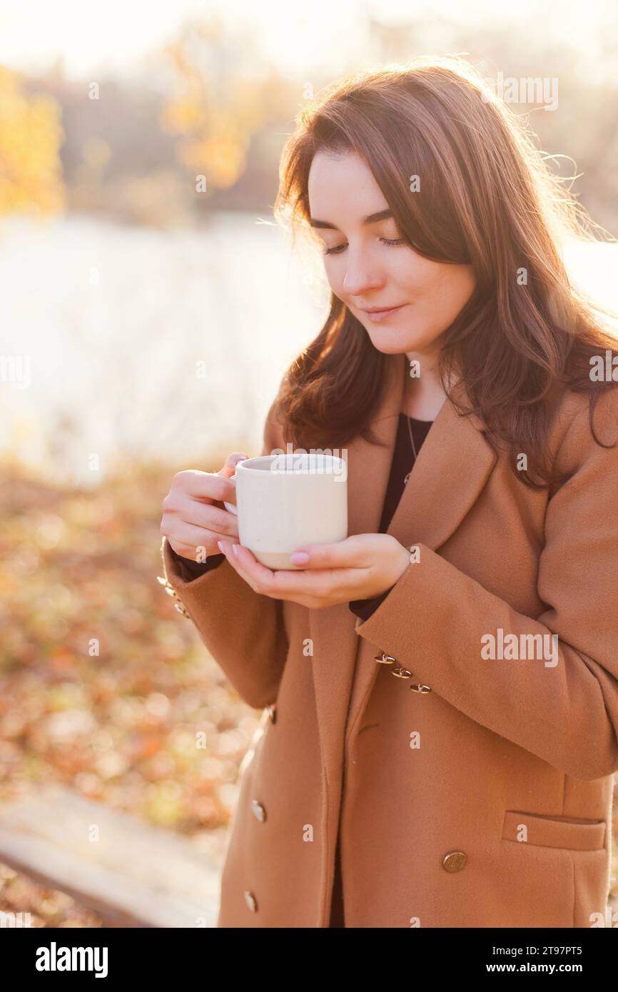 Femme heureuse portant un manteau et tenant une tasse de thé dans le parc d'automne Banque D'Images