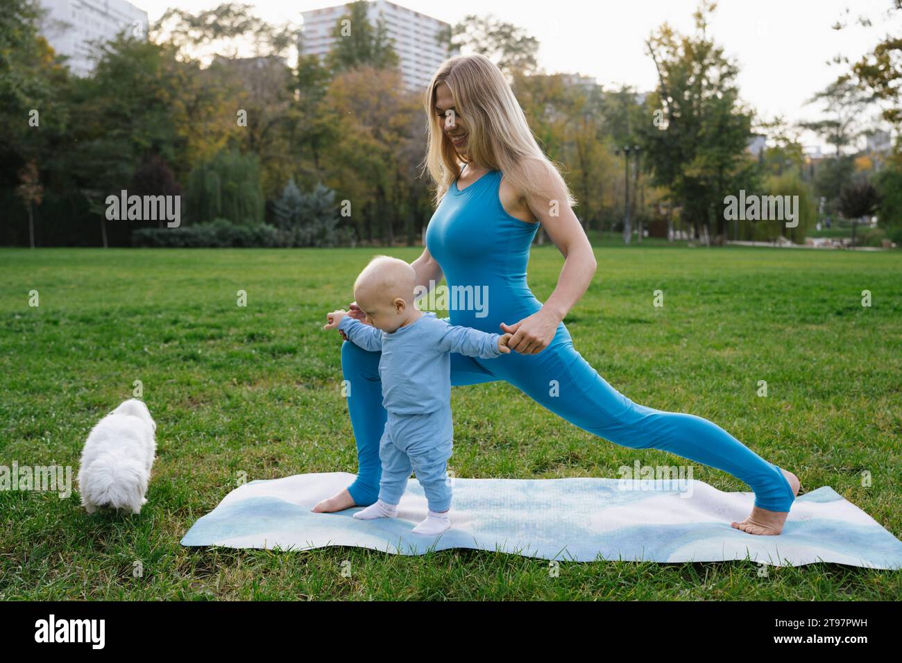 Mère souriante et fils faisant du yoga avec chien dans le parc Banque D'Images