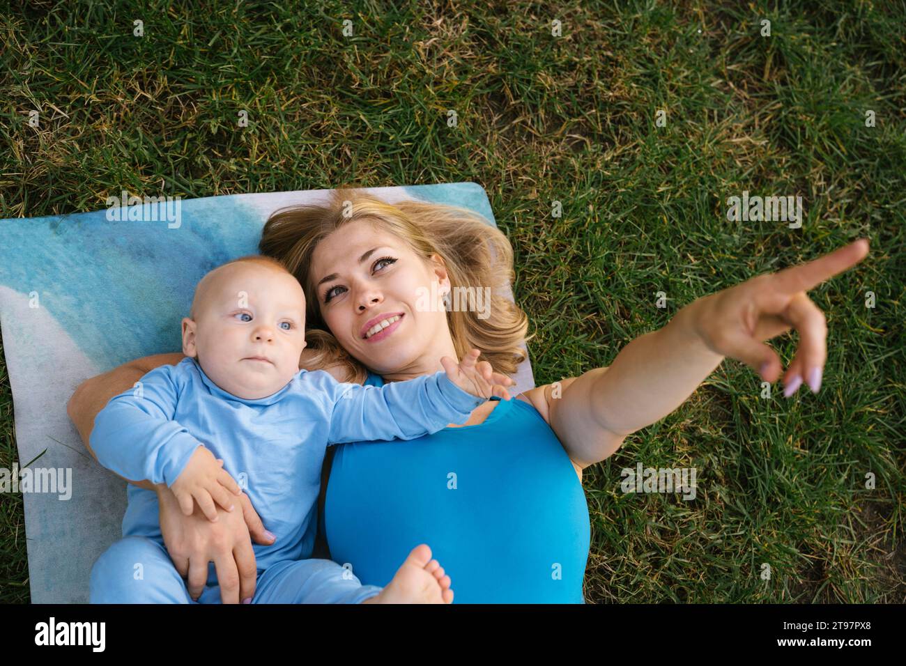 Mère heureuse en gestation et couchée avec son fils sur un tapis d'exercice au parc Banque D'Images