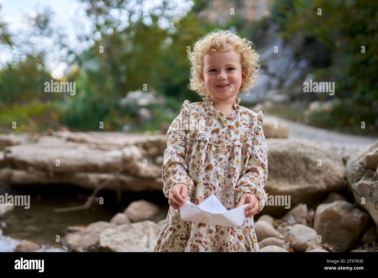 Fille mignonne souriante tenant le bateau de papier devant les rochers Banque D'Images
