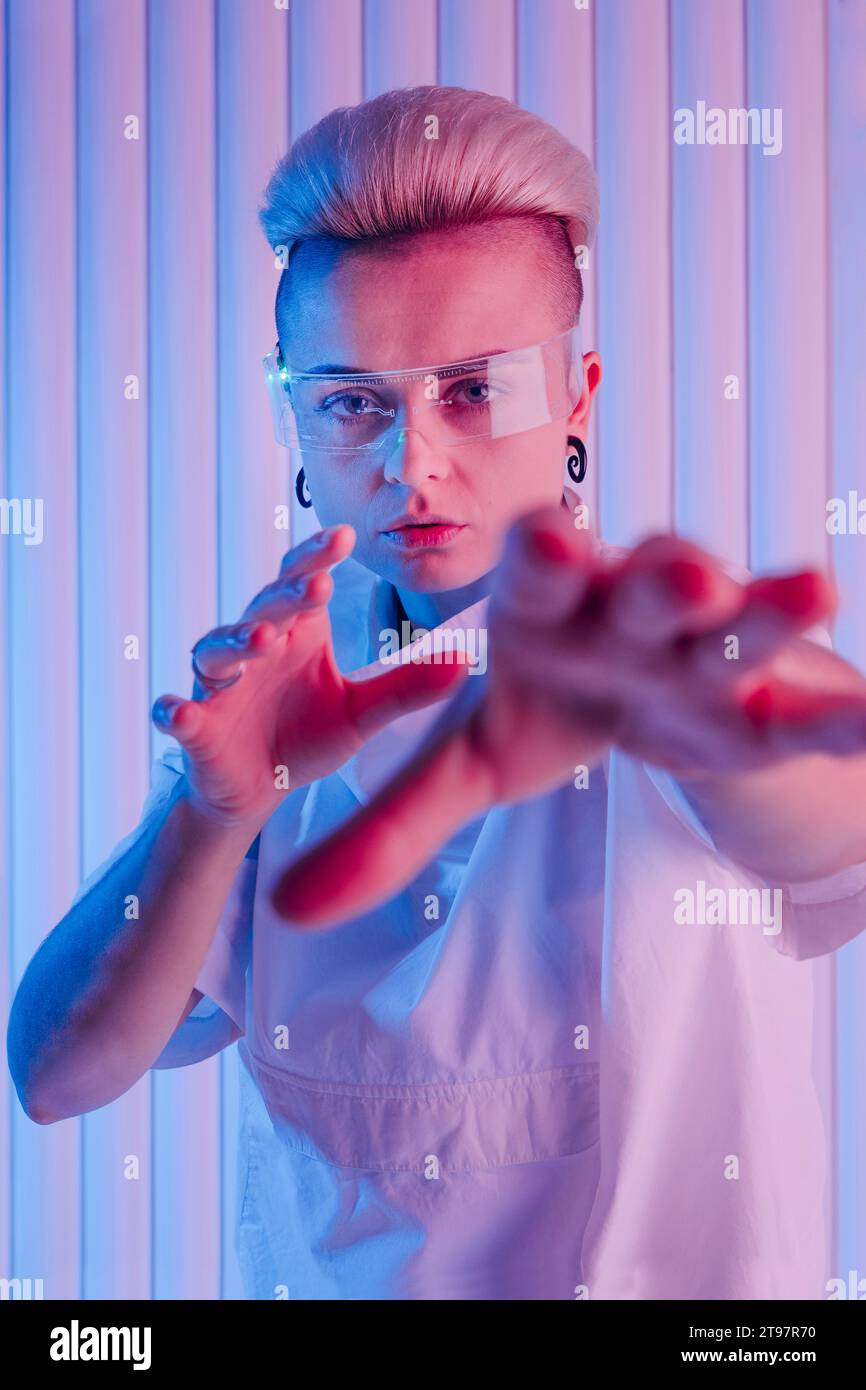 Femme futuriste avec des lunettes intelligentes faisant des gestes devant le mur Banque D'Images