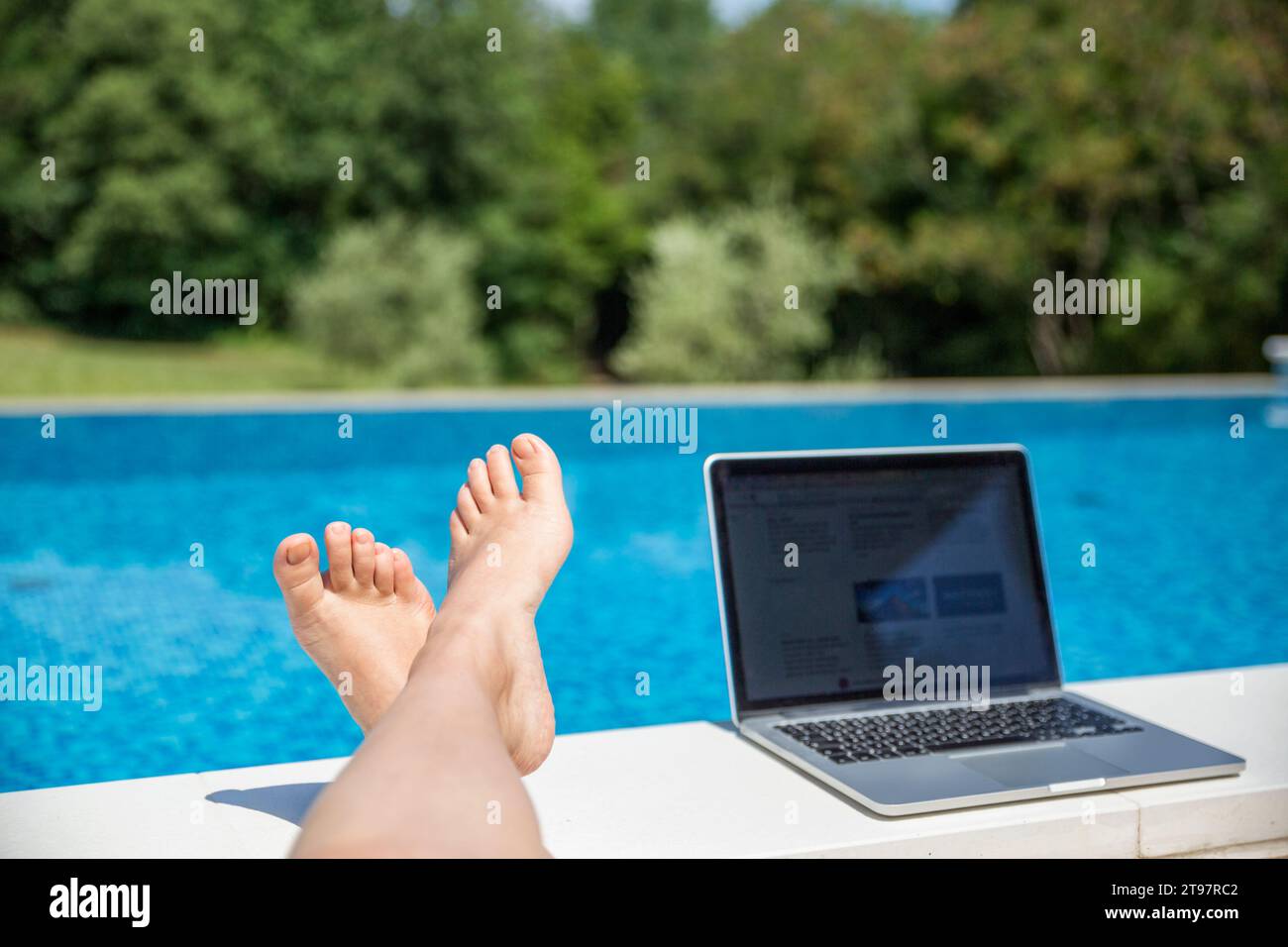 Pied de femme près de l'ordinateur portable au bord de la piscine le jour ensoleillé Banque D'Images