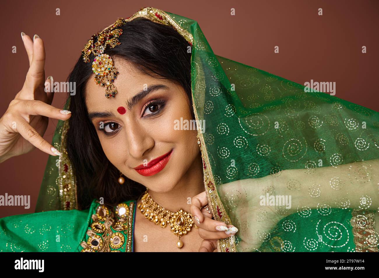jolie femme indienne joyeuse avec bindi dot et voile vert gestionnant et regardant la caméra Banque D'Images