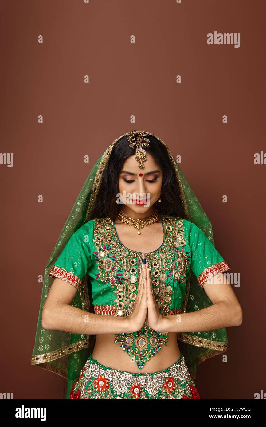 jolie femme indienne avec accessoires et point bindi montrant le geste de prière et regardant vers le bas Banque D'Images