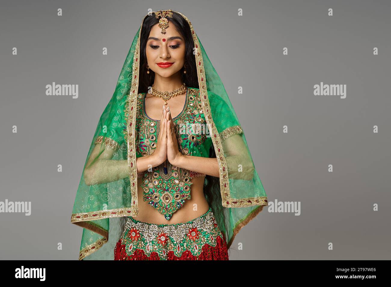 joyeuse jeune femme indienne en costume traditionnel avec voile et bindi priant et regardant vers le bas Banque D'Images