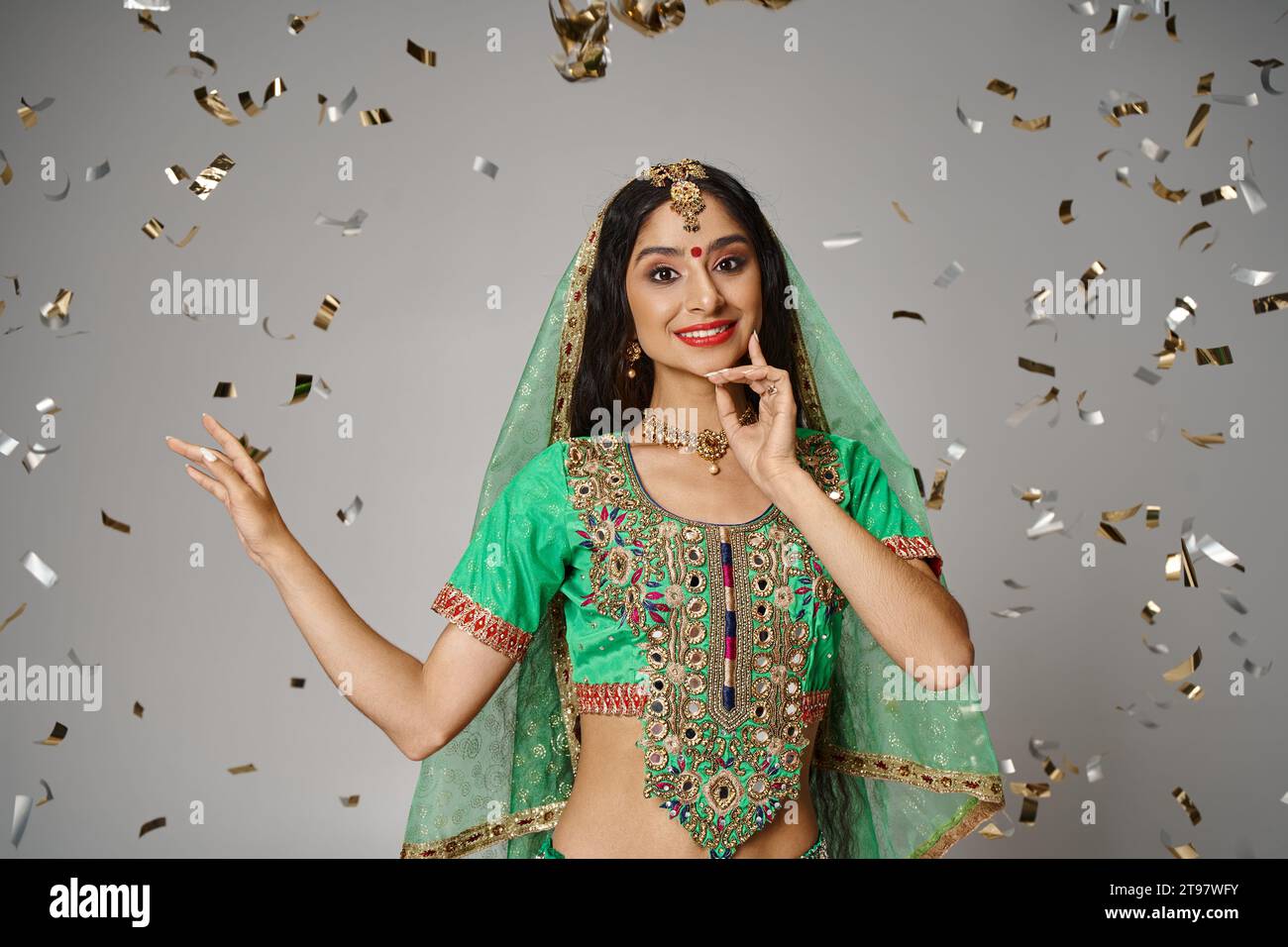 joyeuse jeune femme indienne en vêtements nationaux avec bindi et voile vert entouré de confettis Banque D'Images