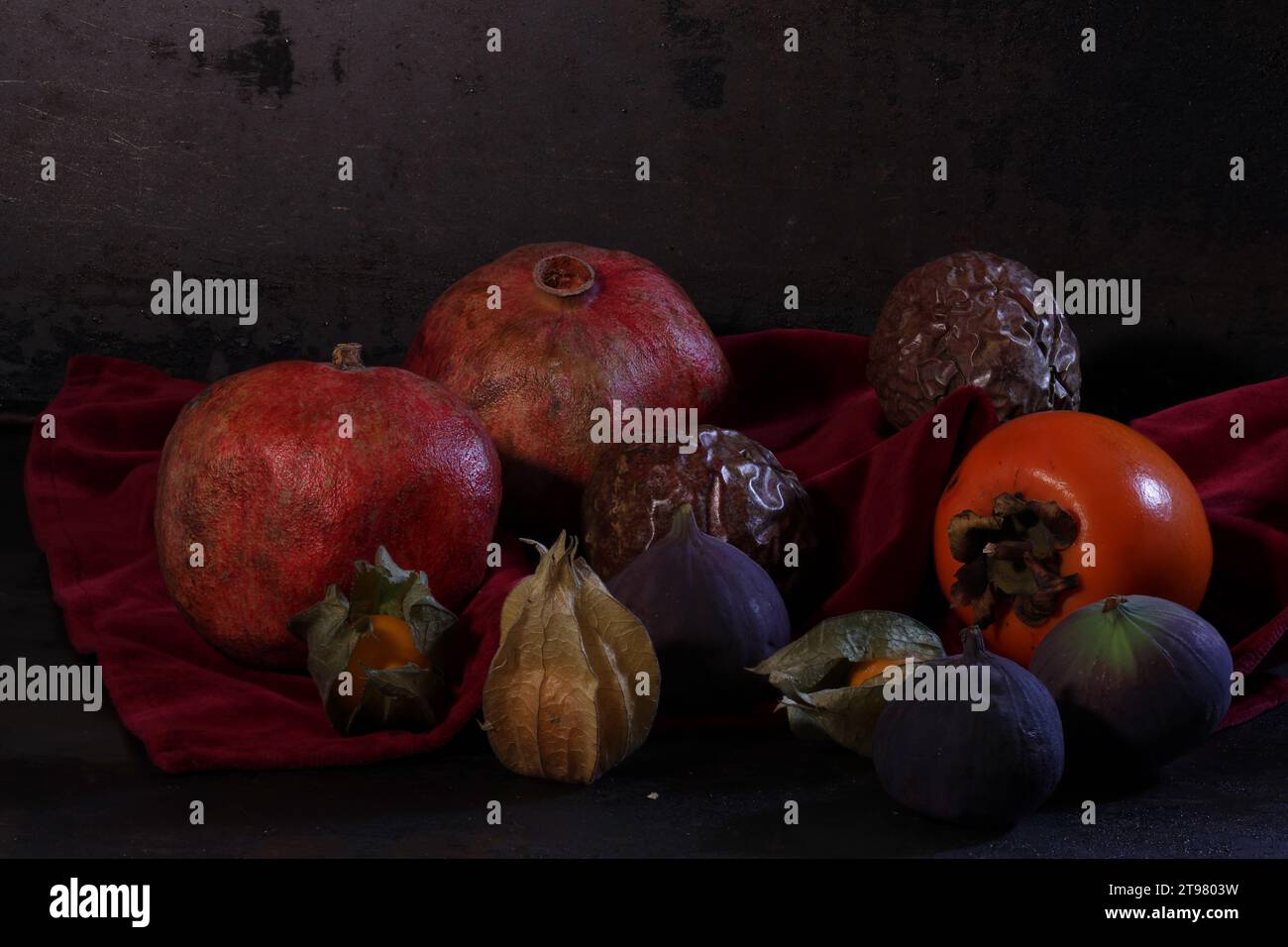 Divers fruits tropicaux et un chardon forment une nature morte sur un tissu de velours rouge foncé. Banque D'Images