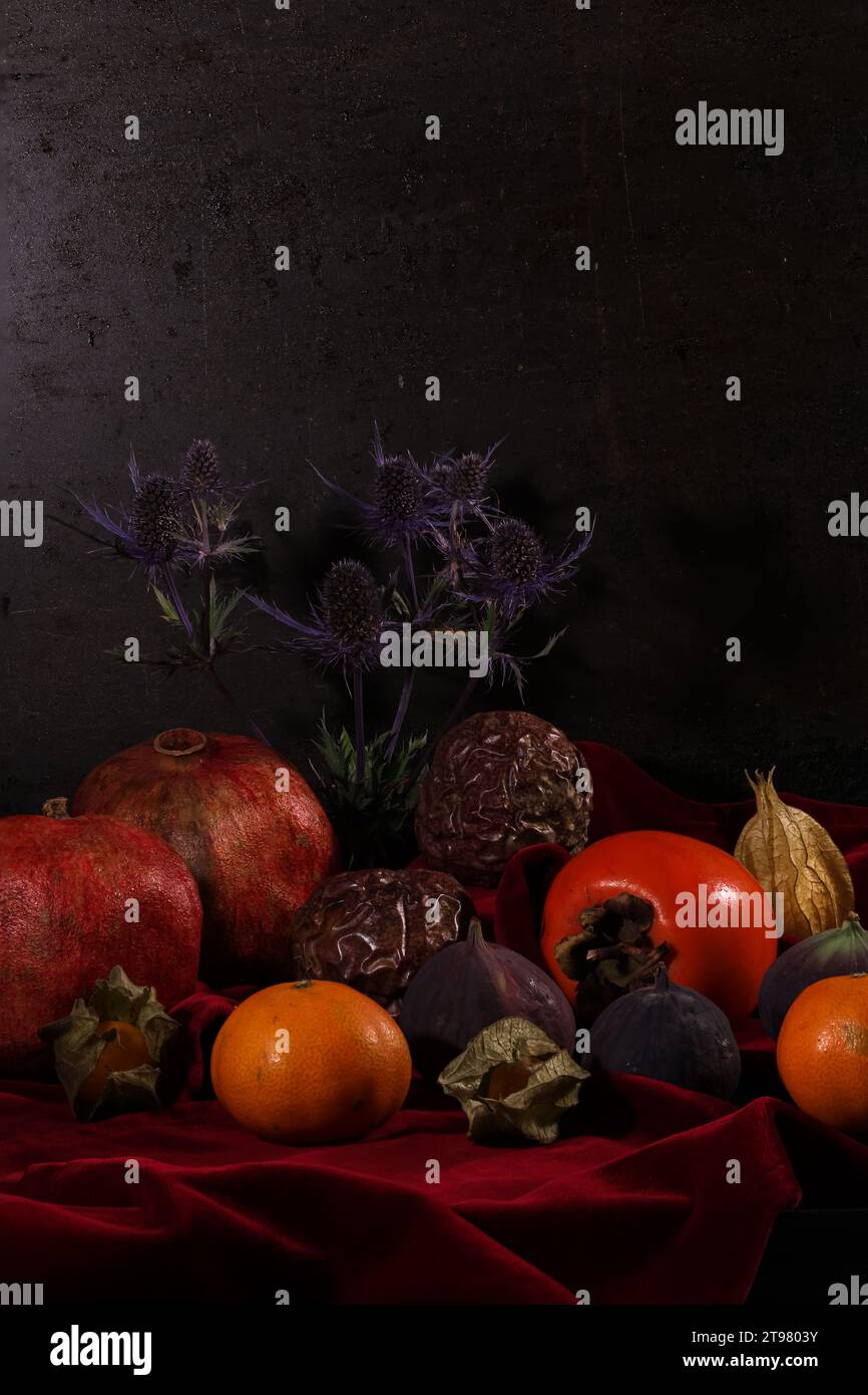 Divers fruits tropicaux et un chardon forment une nature morte sur un tissu de velours rouge foncé. Banque D'Images